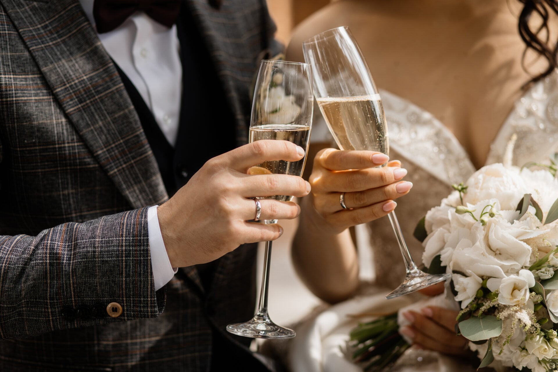 Hände eines Hochzeitspaares mit Sektgläsern und Brautstrauß