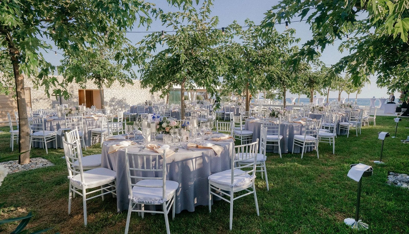 Elegantly set round tables beneath trees in the garden of Coral Residences, with the sea in the background