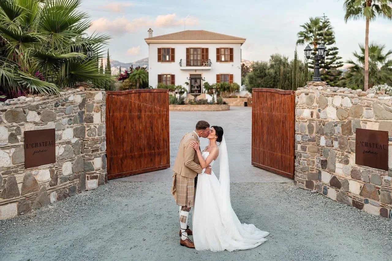 Bride and groom in front of the open gates of the L'Chateau country house in the hills of Tala