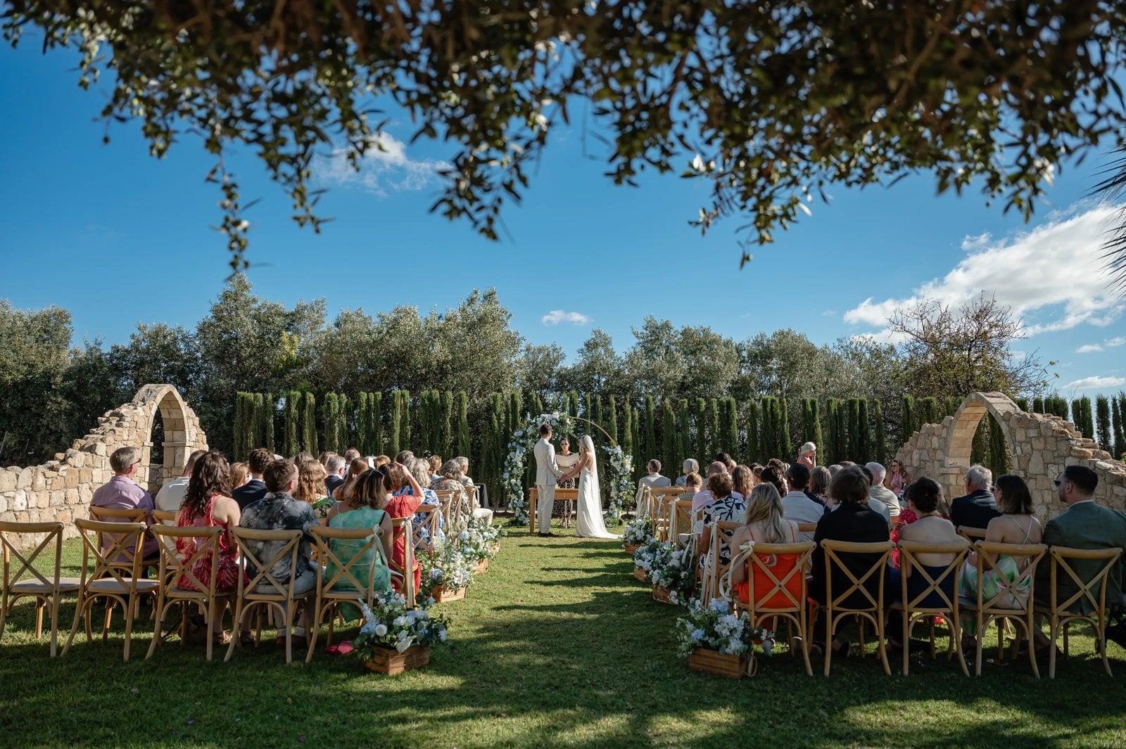 Wedding ceremony on the lawn at L'Chateau between cypresses and old stone arches